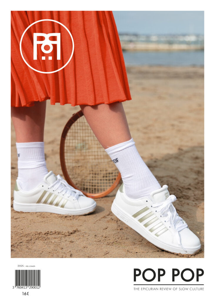 Couverture de la revue épicurienne POP POP. Jambe d'une femme en robe orange, portant des tennis K-Swiss, sur une plage, en fond la mer. En arrière plan des jambes une raquette de tennis ancienne.